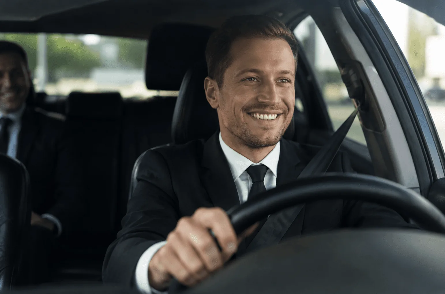 Smiling private chauffeur driving a Mercedes in Helsinki with a passenger in the back seat
